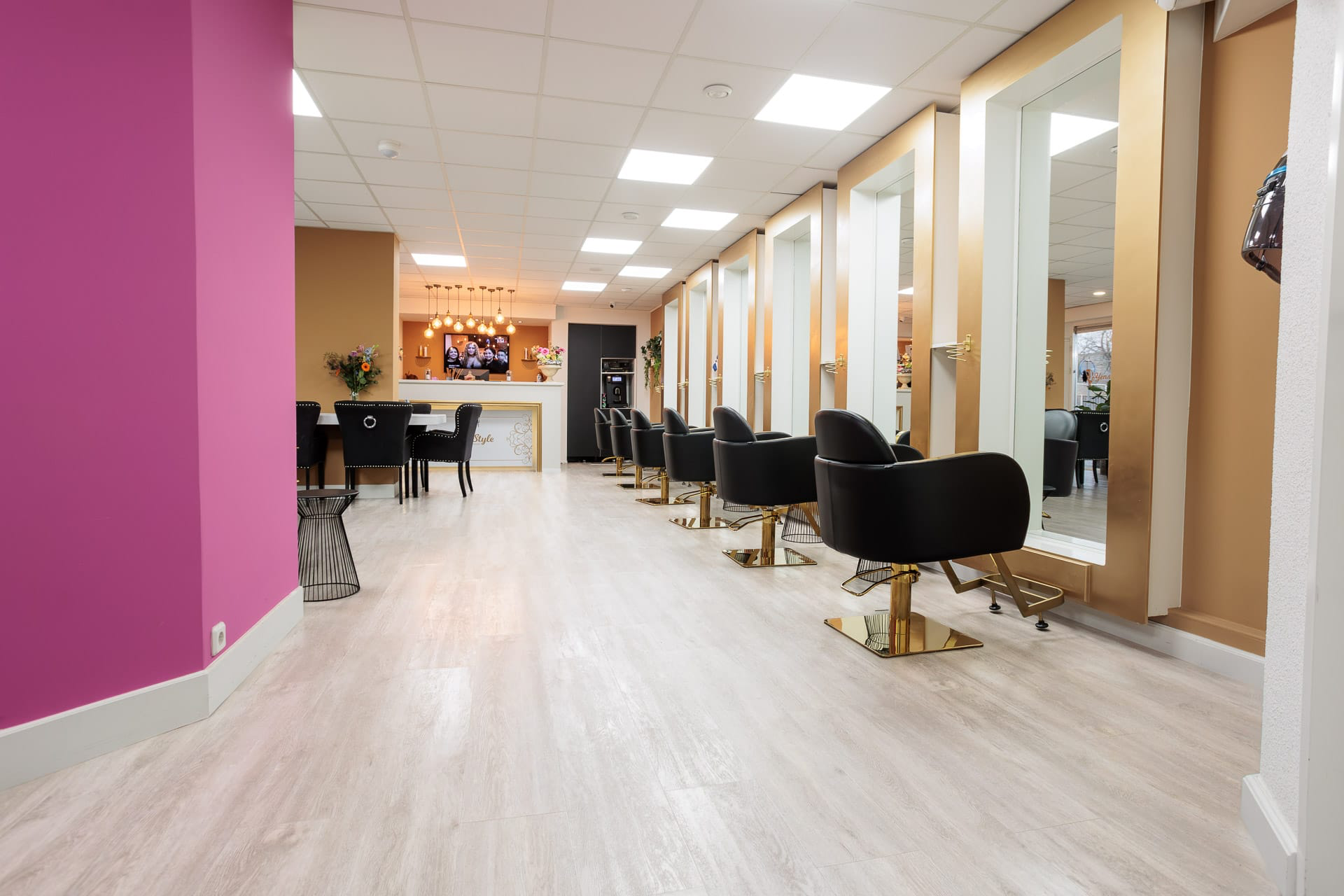 Ruime salon van Yensi Style met roze accentmuur, gouden spiegels en zwarte stylingstoelen